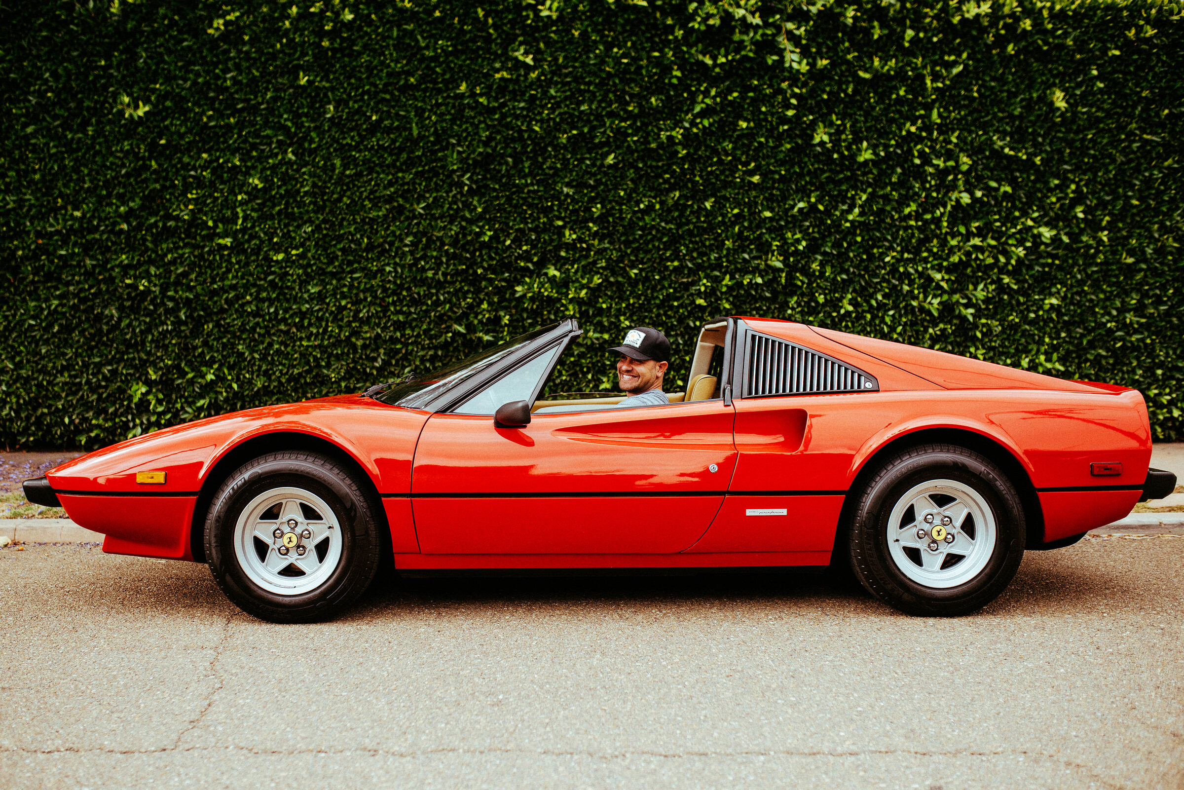 Adam Moyer in a red Ferrari 308 in front of an ivy wall